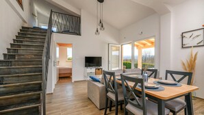 A modern interior with a staircase, a dining area with a table and chairs, a sofa, and a TV. - Beautiful home in Krsan (Krsan)