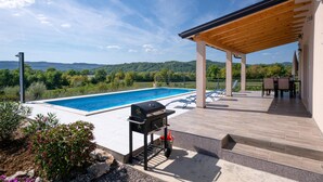 A poolside area with a wooden deck, a barbecue grill, and a view of the countryside. - Beautiful home in Krsan (Krsan)