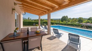 A covered outdoor area with a pool, a dining table with chairs, and a view of the surrounding landscape. - Beautiful home in Krsan (Krsan)