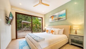 A bedroom with a large bed, a nightstand, a ceiling fan, a painting, and a view of a patio with outdoor furniture. - 3 King Suites | Pool, Outdoor Oasis | Casa Coralis (Potrero)
