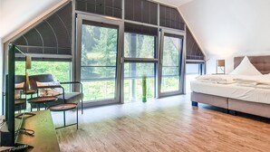 Um quarto moderno com uma janela grande, uma cama e um espaço de estar com mesa e cadeiras.
