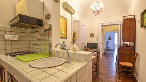 Eine Küche mit Gasherd, Spüle und einer grünen Schneidebrett. Eine Kronleuchter hängt von der Decke und es gibt einen Essbereich mit Stühlen und einem Tisch.