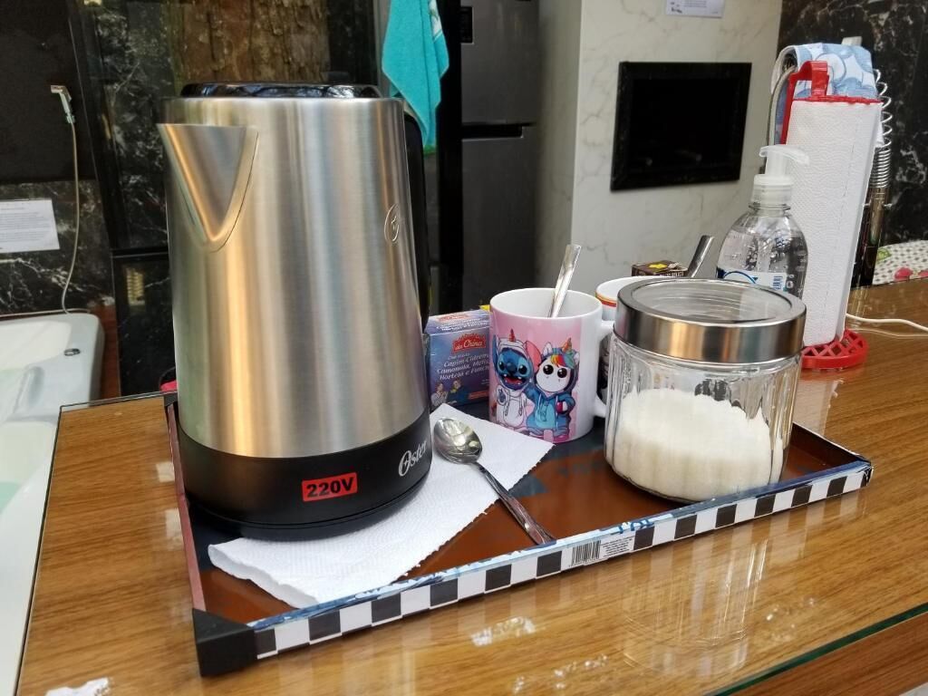A kitchen counter with a stainless steel kettle, a mug, a container of sugar, and a bottle of water.