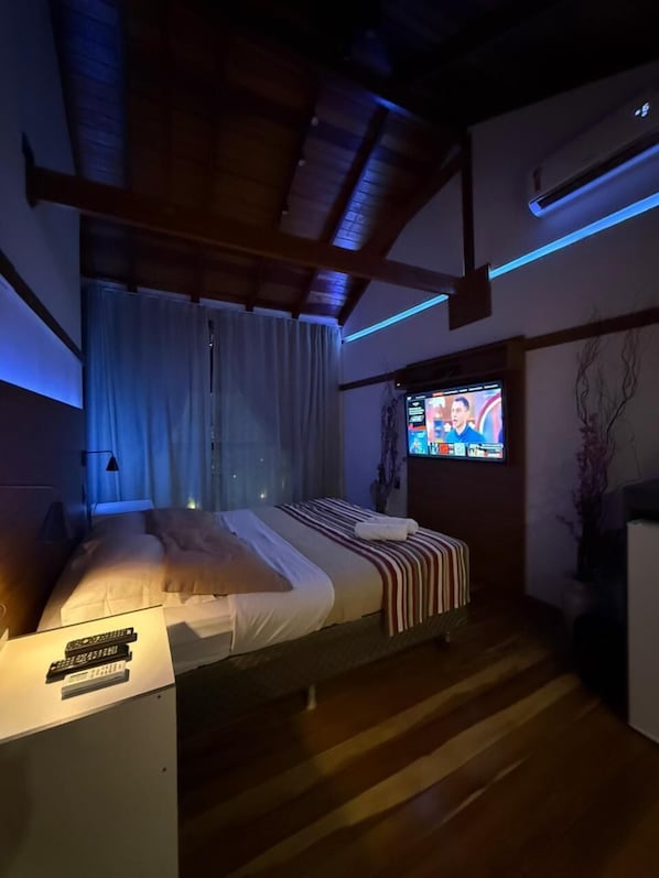 A modern bedroom with a bed, a TV mounted on the wall, and a wooden ceiling.