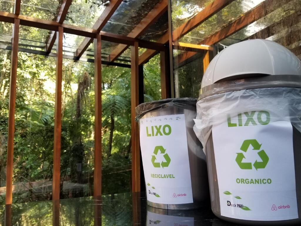 Dos contenedores LIXO para reciclaje con cerramiento de vidrio y estructura de madera, frente a un fondo de vegetación.