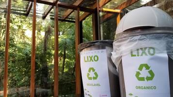 Dos contenedores LIXO para reciclaje con cerramiento de vidrio y estructura de madera, frente a un fondo de vegetación.