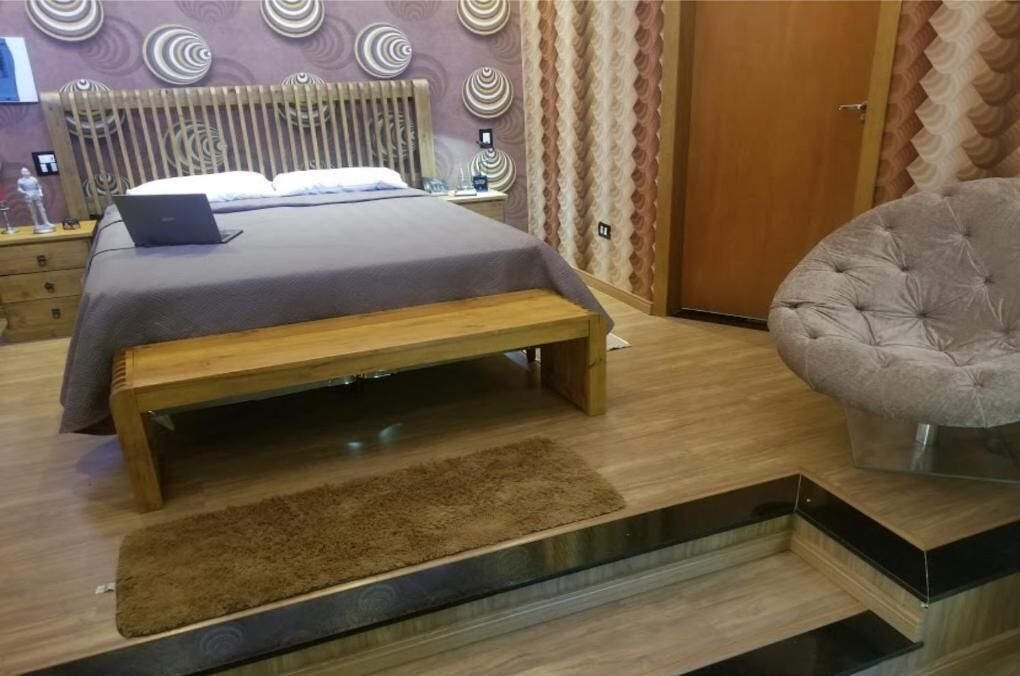 Un dormitorio moderno con una cama, un ordenador portátil sobre la cama, un banco y un sillón tapizado.