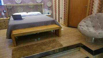 Un dormitorio moderno con una cama, un ordenador portátil sobre la cama, un banco y un sillón tapizado.