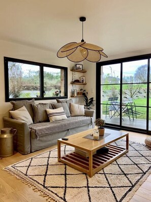 Ein gemütliches Wohnzimmer mit einer Couch, einem Couchtisch und einem großen Fenster mit Blick ins Freie.