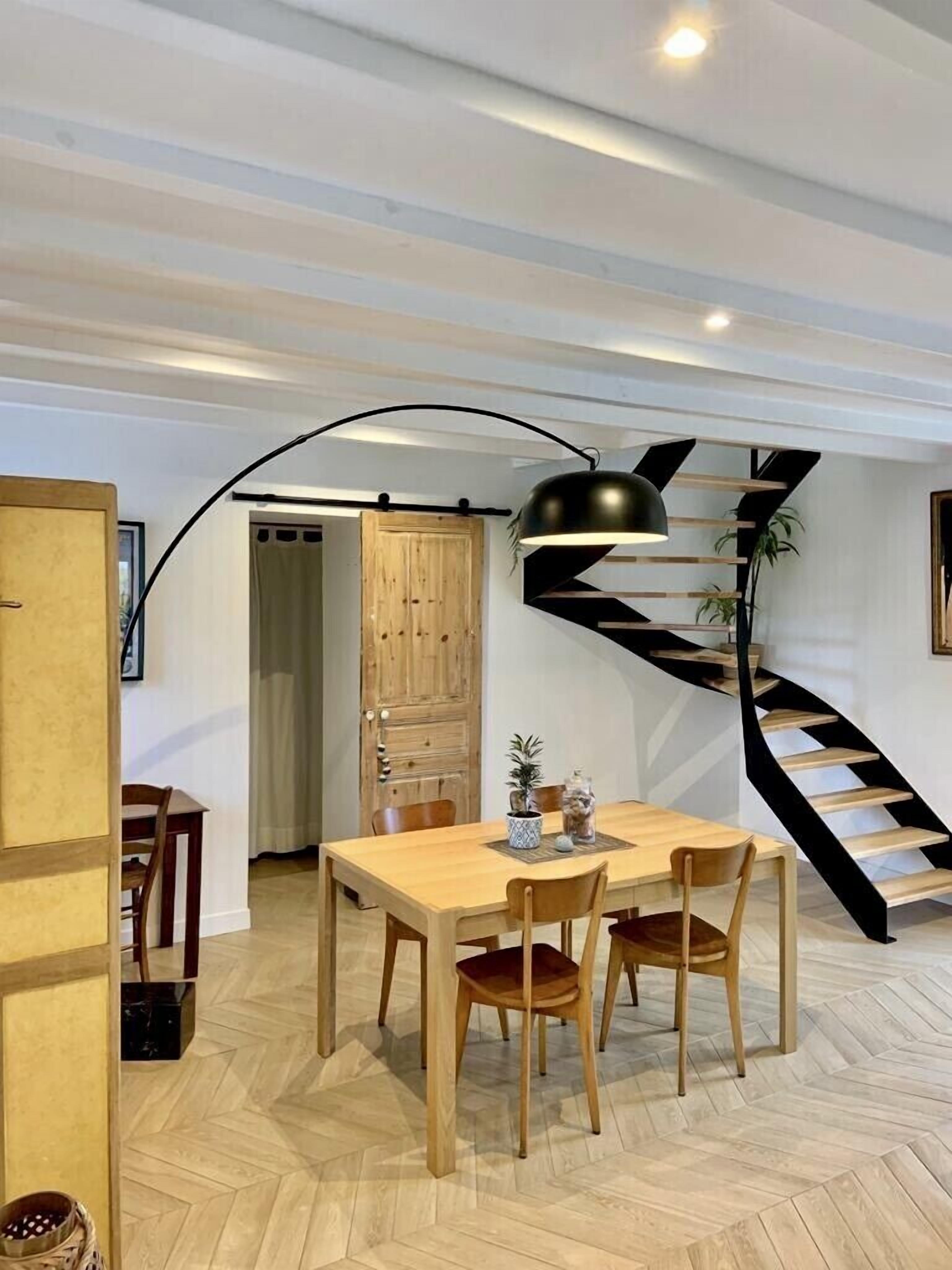 Un espace repas avec une table et des chaises en bois, un escalier en colimaçon noir et un luminaire suspendu moderne.