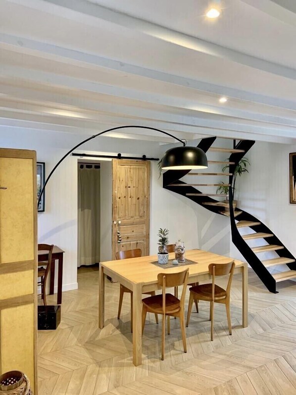 Ein Essbereich mit Holztisch und -stühlen, einer schwarzen Wendeltreppe und einer modernen Pendelleuchte.
