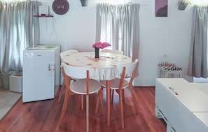 A dining area with a round table, chairs, a refrigerator, a chessboard, and curtains.