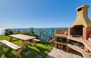 An outdoor patio with a wooden table and benches, a brick barbecue grill, and a view of the sea. - 2 bedroom awesome home in Cipressa (Cipressa)