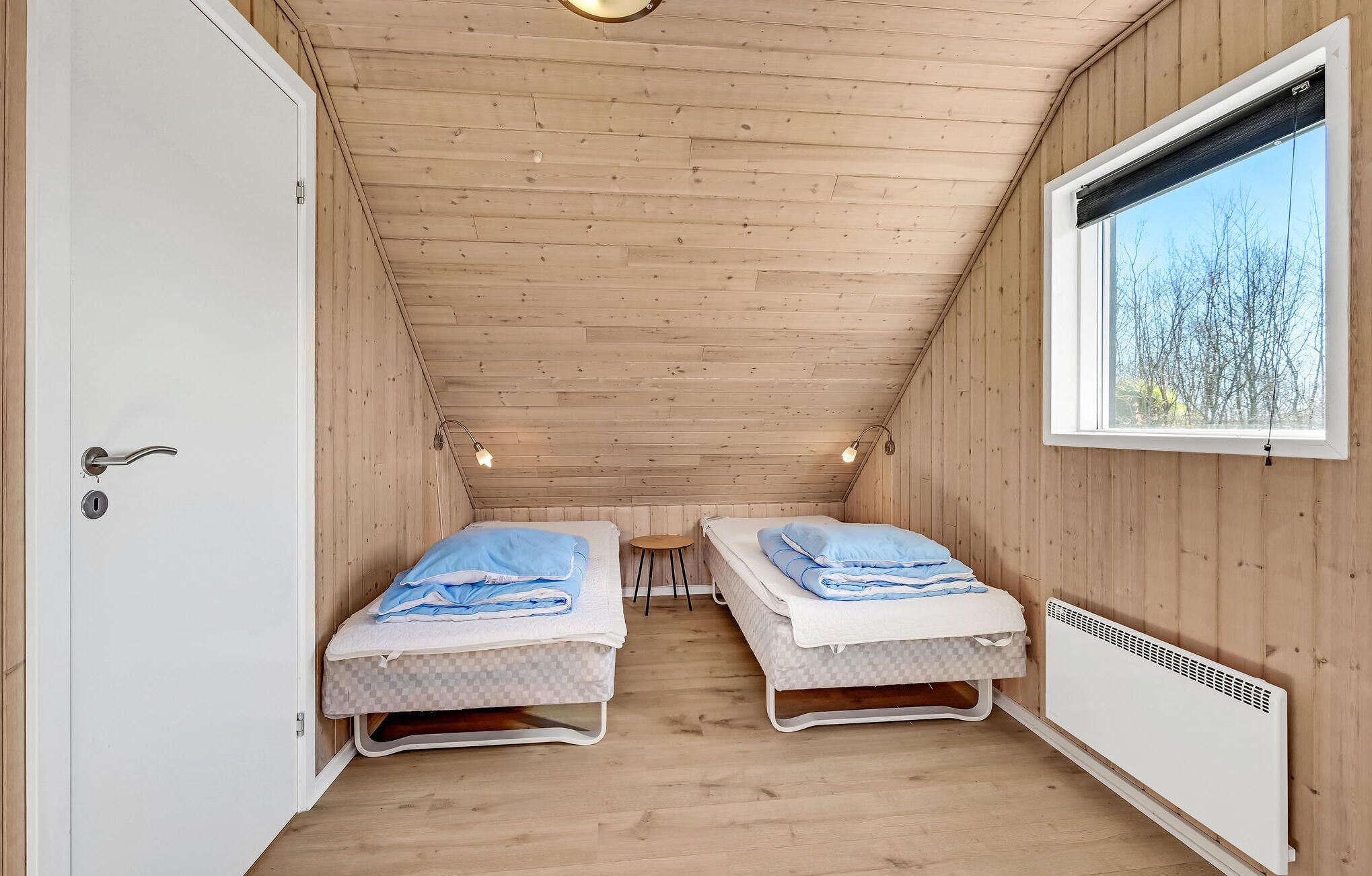 A small, wooden cabin room with two beds, a window with a view of trees, and a white door.