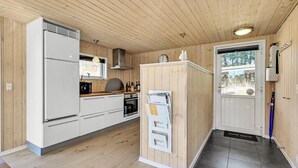 Une cuisine compacte équipée d’un réfrigérateur Bosch, d’un four à micro-ondes et d’une cuisinière. On y trouve un meuble en bois avec une fenêtre, ainsi qu’une porte donnant sur l’extérieur.