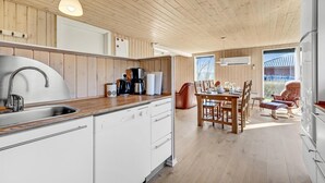 Une cuisine moderne avec un lambris en bois, un évier en acier inoxydable et un coin repas comprenant une table et des chaises.