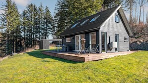 Une cabane moderne dotée d’une terrasse, de grandes fenêtres et d’un espace salon extérieur abrité.