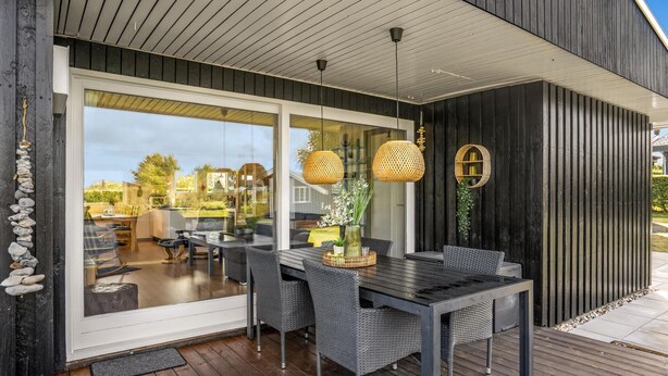 A modern outdoor dining area with a glass wall, wicker furniture, and hanging rattan lamps. - Beautiful home in Glesborg with kitchen (Glesborg)
