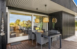 Et moderne udendørs spiseområde med glasvæg, fletmøbler og hængende rattanlamper.