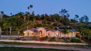 Ein zweistöckiges Haus mit einer großen Veranda, Solaranlage und Auffahrt.