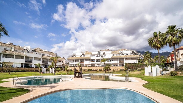 Ein Resort mit zwei Schwimmbecken, einem gepflegten Rasen und weißen Gebäuden im Hintergrund, die Balkone aufweisen.