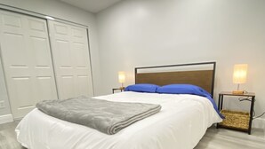 A neatly made bed with a white comforter and a gray throw blanket, two bedside lamps, and a wooden headboard. - FL Beach Get-Away! 1BD/1BA in 2BD/2BA Available in South Florida (Delray Beach)
