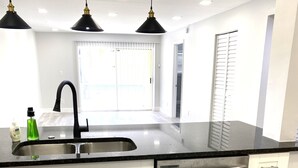 A modern kitchen with a stainless steel sink, white cabinets, a dishwasher, and pendant lighting. - FL Beach Get-Away! 1BD/1BA in 2BD/2BA Available in South Florida (Delray Beach)