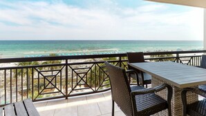 Varanda com vista para a praia, móveis de vime e uma mesa.