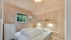 A wooden-paneled bedroom with a bed, a dresser, a window, and a shelf with decorative items. - Gorgeous home in Hemmet with sauna (Hemmet)