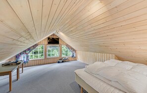 Une chambre mansardée chaleureuse, avec un plafond en pente, un lit, un bureau et une fenêtre donnant sur un paysage verdoyant.