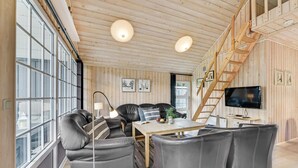A cozy living room with a sofa, chairs, a table, and a TV. There are wooden walls and a staircase. - Gorgeous home in Hemmet with sauna (Hemmet)