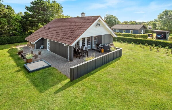 Une maison de plain-pied avec un toit en pente, une terrasse dotée de mobilier d’extérieur et une cour clôturée.