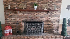 Una chimenea de ladrillo con árboles decorativos, un florero blanco y una planta en maceta sobre la repisa.