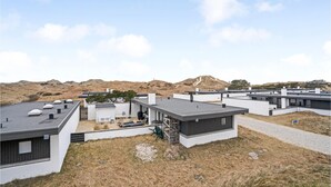 Ein moderner Wohnkomplex mit mehreren Häusern, die sich durch flache Dächer und große Fenster auszeichnen, vor einer hügeligen Landschaft.
