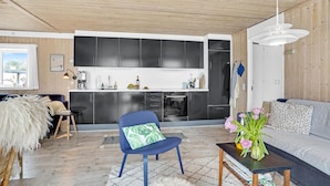 Eine moderne Küche mit dunklen Schränken und einer weißen Arbeitsplatte, ein blauer Stuhl mit grüner Sitzkissen, ein graues Sofa und eine Holzbalkendecke.