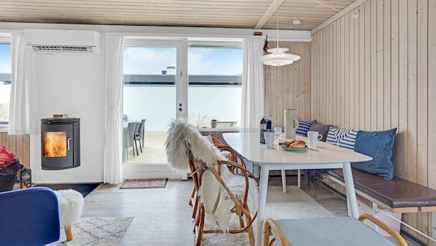 Ein gemütliches Zimmer mit Holzbalkendecke, einem weißen Tisch mit blauen Kissen, einem weißen Hund und einem Kaminofen.