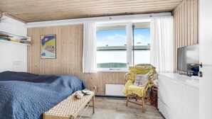 Ein Schlafzimmer mit Bett, Sessel, Bank, Fernseher und einem Fenster mit Vorhängen.