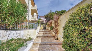Un étroit sentier de pierre mène à un bâtiment à la façade blanche et doté de balcons.