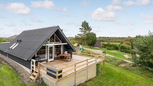 A modern house with a sloped roof, a wooden deck, and a large glass door leading to an outdoor area. - Stunning home in Roslev with WiFi (Roslev)
