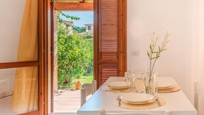 A dining area with a table set for four, a wooden door leading to a garden, and a vase with flowers on the table. - Beautiful apartment in San Teodoro (San Teodoro)