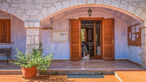 A building with a stone facade, wooden shutters, and a tiled entrance. A dog is visible at the entrance. - Beautiful apartment in San Teodoro (San Teodoro)