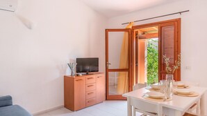A compact room with a wooden cabinet, a television, a dining table set with plates and glasses, and a blue sofa. - Beautiful apartment in San Teodoro (San Teodoro)