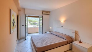 Un dormitorio con cama, mesita de noche, lámpara de pared y vistas a un espacio exterior por una puerta.