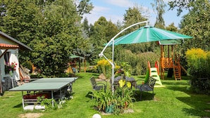 Un jardin avec une table de ping-pong, des chaises, une table ornée d’une plante, un ballon de foot et une balançoire.