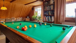 Une table de billard dans une pièce aux murs en bois et une bibliothèque remplie de livres.