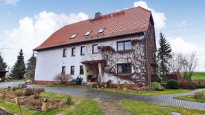 Une maison à deux étages, avec un toit recouvert de tuiles rouges, de nombreuses fenêtres et un jardin agrémenté d’une allée pavée.