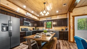 A modern kitchen with wooden cabinets, stainless steel appliances, and a dining area with a bench and chairs. - ★Modern★ Family Friendly Cabin in Pigeon Forge - Hot Tub Game Room Fire Pit (Pigeon Forge)