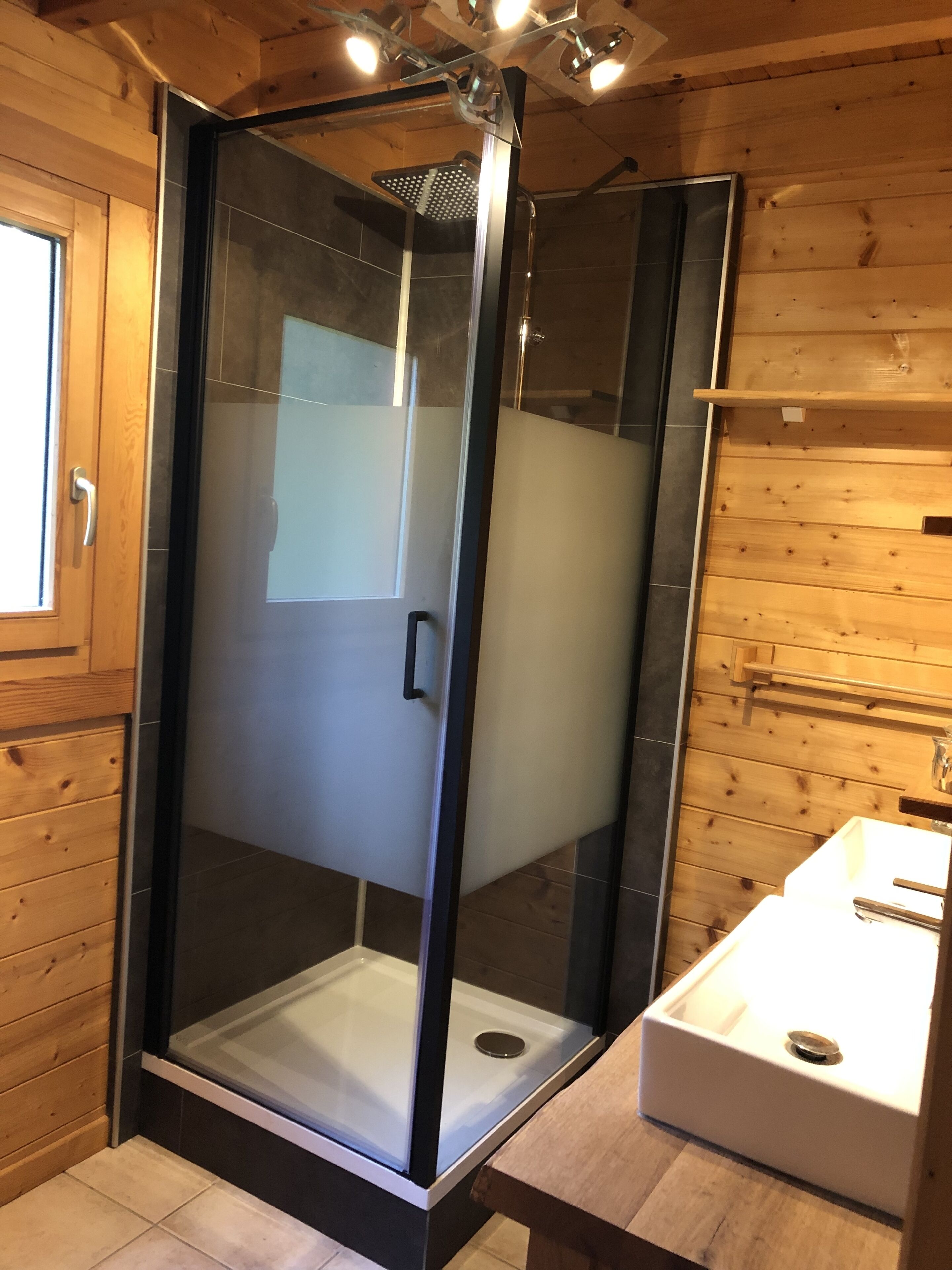 Une salle de bain moderne avec une douche à parois de verre, un lavabo blanc et un lambris en bois.
