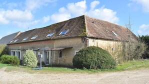 Un edificio rustico a un piano con tetto spiovente, diverse finestre a lucernario e un piccolo portico.