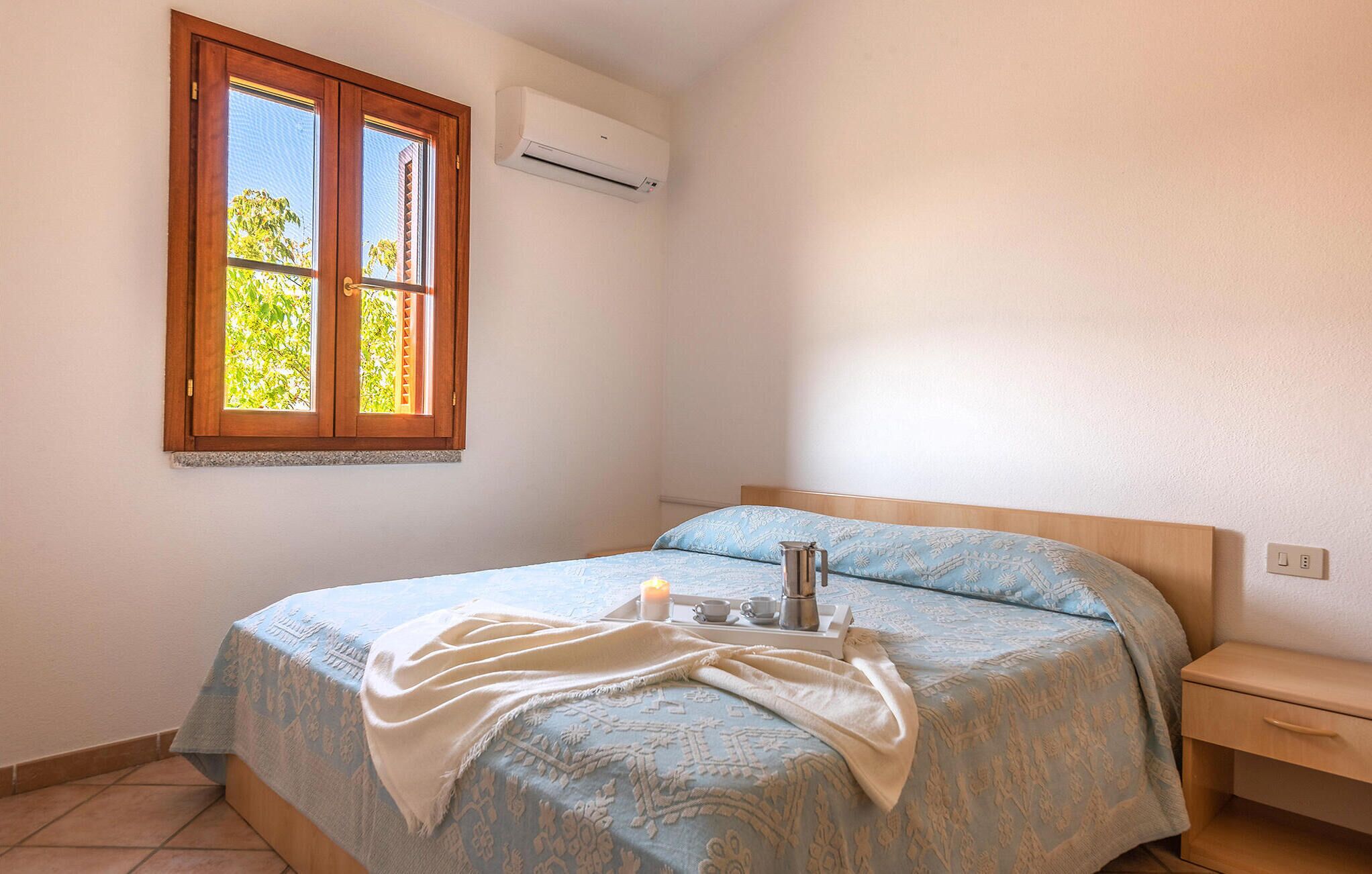 Une chambre à coucher comprenant un lit, une table de chevet, une commode, une fenêtre et un appareil de climatisation.